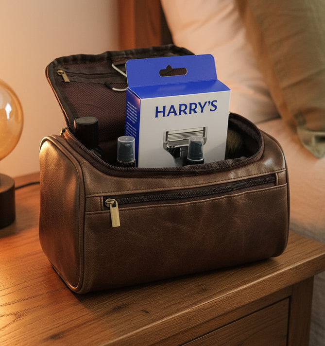 Brown toiletry bag with Harry's razor and other items on a white surface